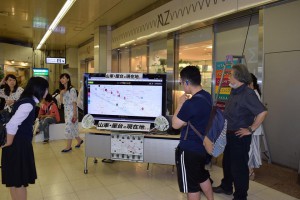 熊谷駅コンコースで出し位置を説明する立正大生。